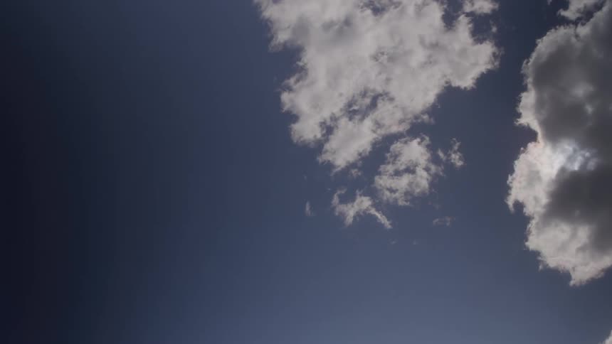 Blue sky with white and gray clouds partially covering the sun