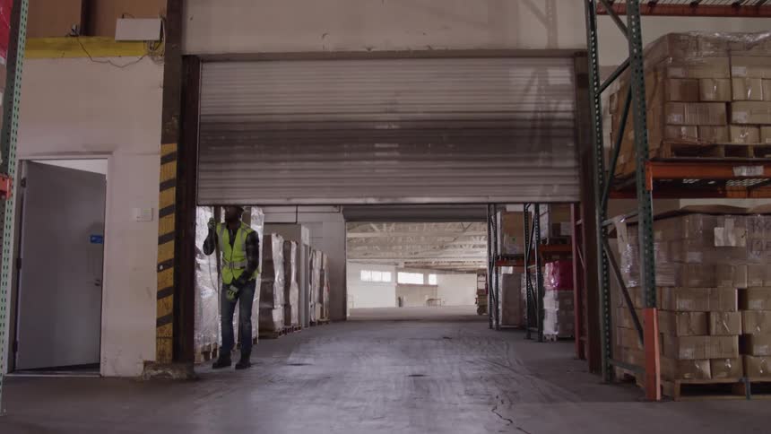 Worker wearing a reflective vest and hard hat pulling down a warehouse rollup door