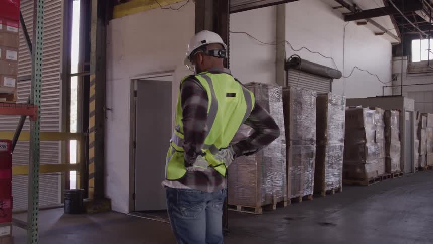 A young black male worker stretches his back while standing in a warehouse during daytime