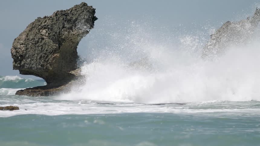 A large wave crashes over rocky outcroppings in the ocean
