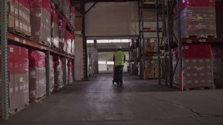 Worker wearing a reflective vest pushing a hand truck through a warehouse aisle