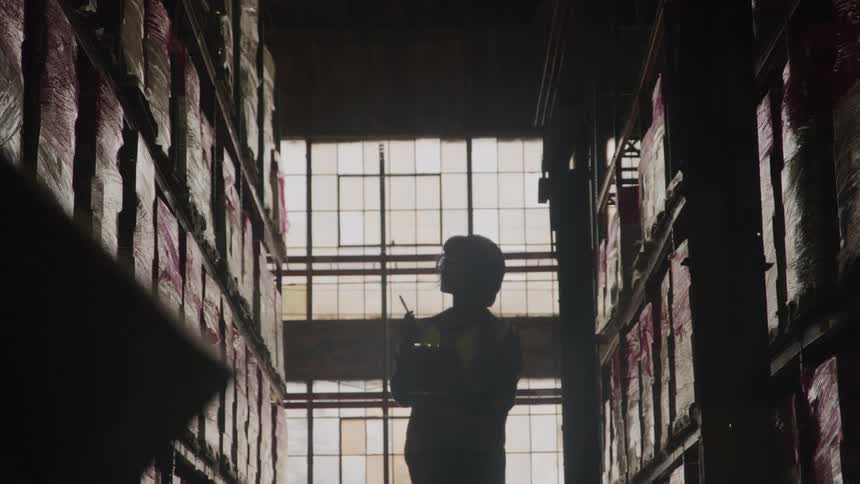 Silhouette of a female worker wearing a hard hat walking between warehouse shelves