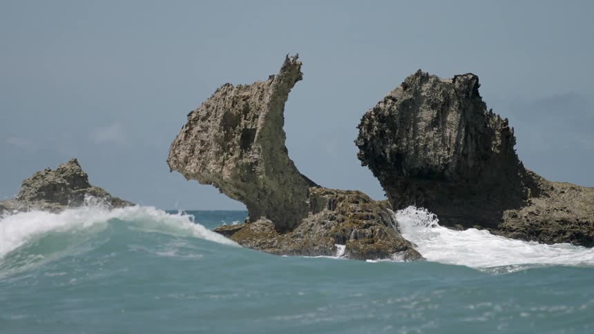 Waves crash against a row of rocks by the shore
