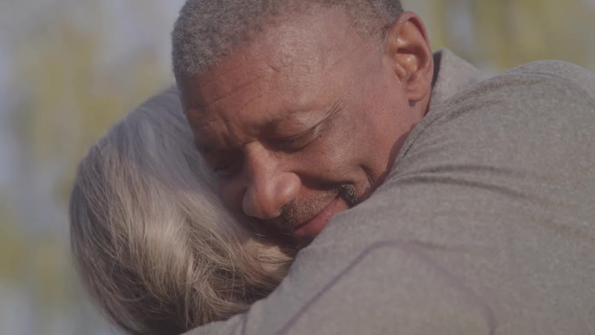 A man hugs a woman outdoors smiling at midday