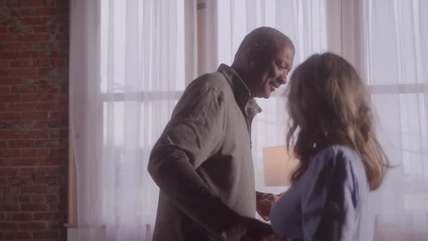 Older couple smiling and dancing together in a room lit by natural light
