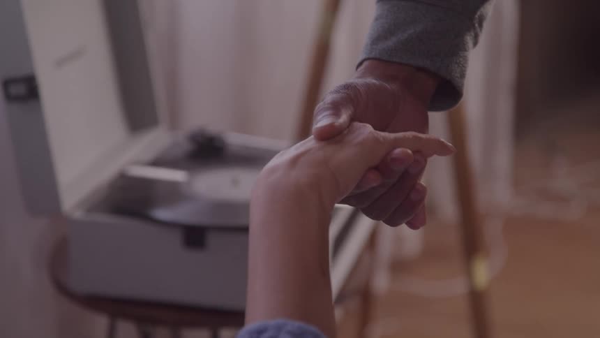 Two hands holding each other with a record player in the background