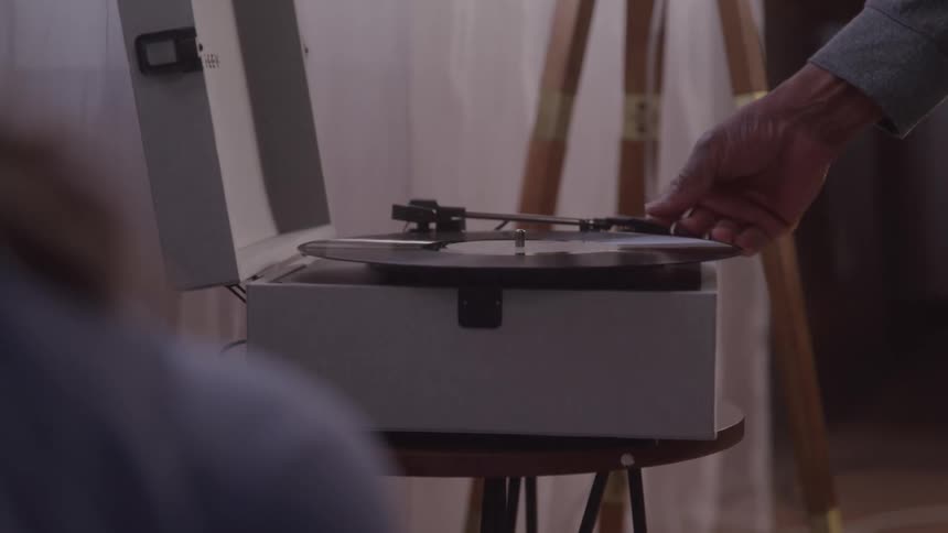 A man is placing a black vinyl record onto a portable record player