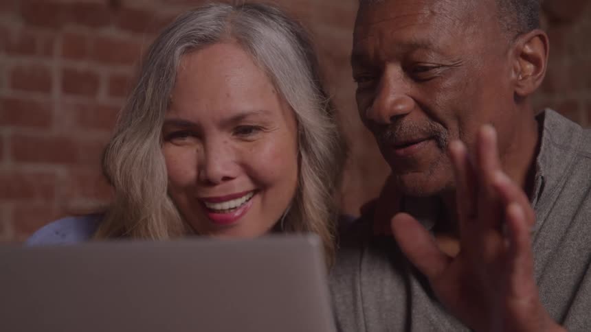 Close up of an elderly couple together on a video call with a laptop computer while seated in a room during daytime