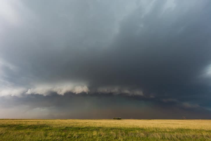 Storm clouds gather then flow over a grassland during the daytime