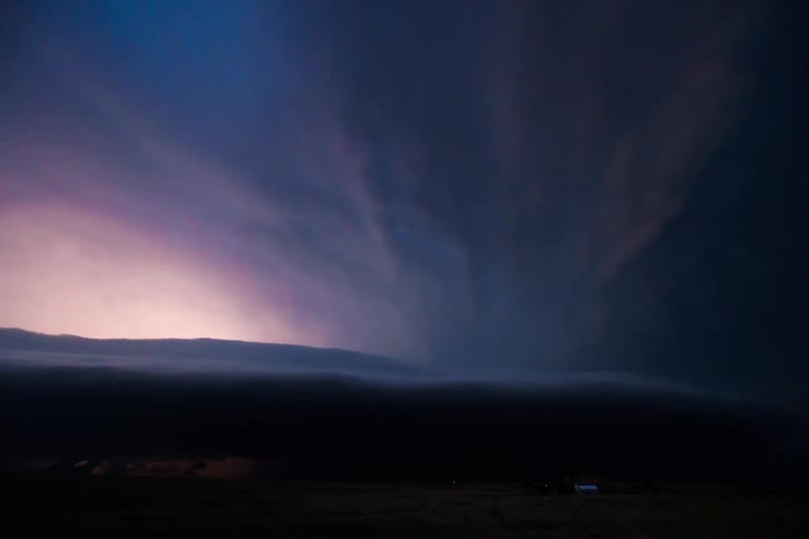 A dramatic thunderstorm cloud formation glows from lightning at the horizon during twilight