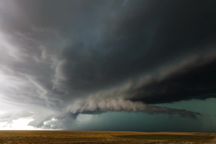 Dark storm clouds gather and start to twist slowly above a grassland during the daytime