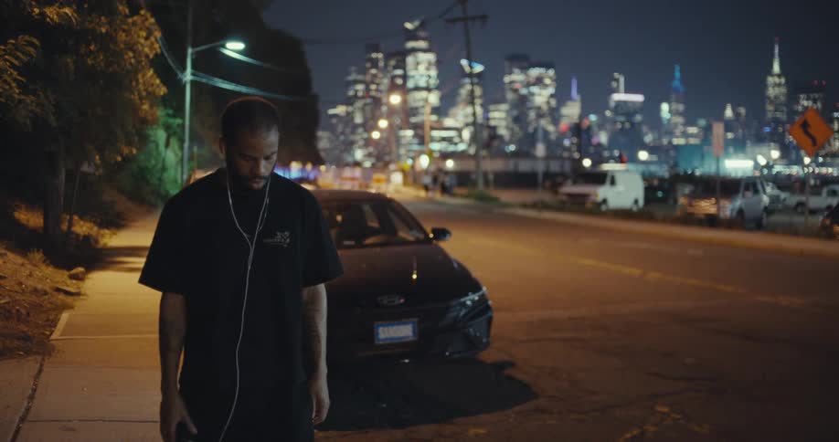 Man stands on the sidewalk at night with the city lights in the background