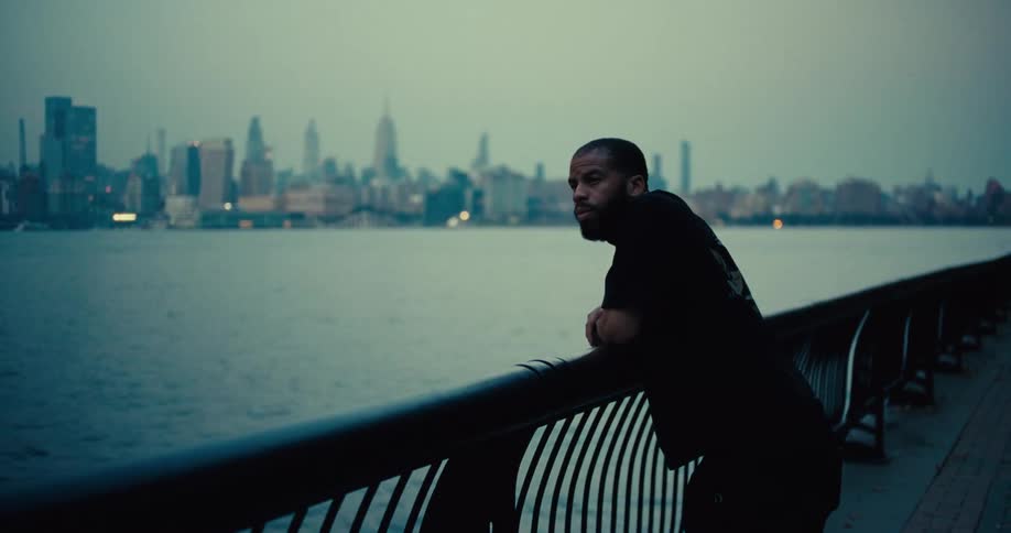 Man leans on railing overlooking city skyline at dusk