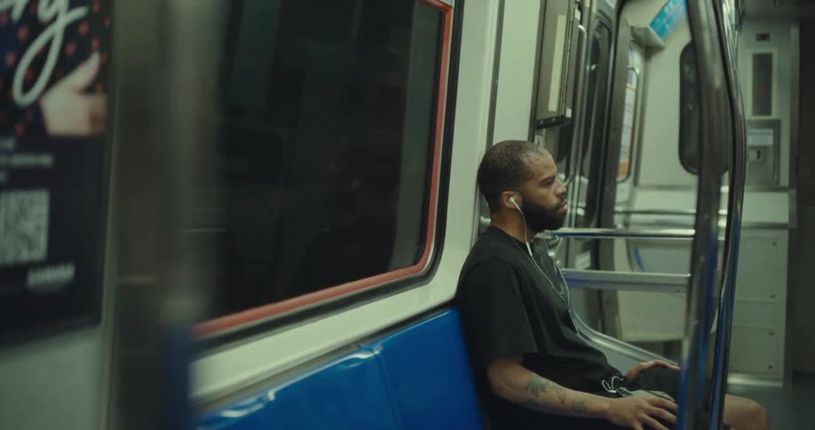 Man sits alone on a subway seat wearing earphones
