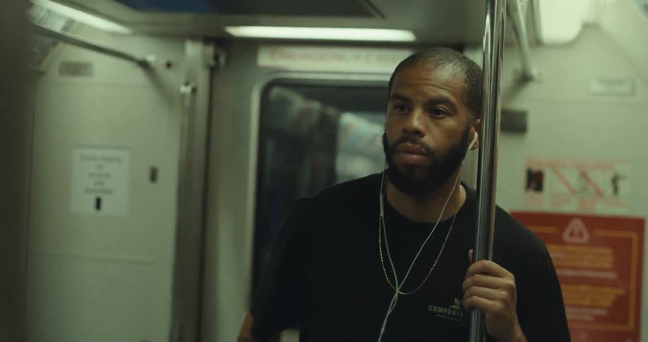 A man with earphones stands holding a subway pole appearing tired during a train ride