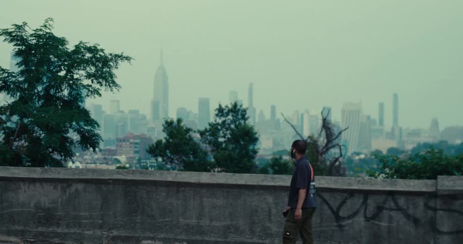 A man stands by a graffitimarked wall gazing at the hazy new york city skyline in the distance
