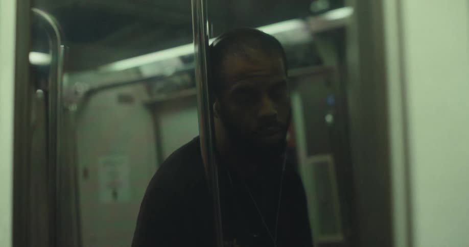 A man wearing earphones is dimly reflected in a subway doors glass during a train ride