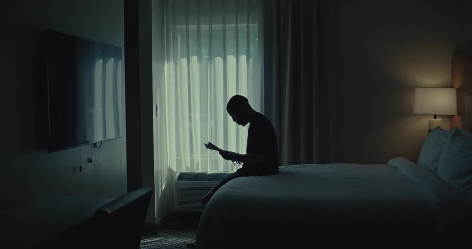 Silhouette of a man sitting on the bed in a bedroom reading documents