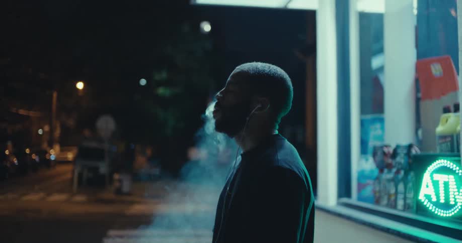 A man on the street lighting a cigarette with a lighter then smoking and blowing the smoke upward