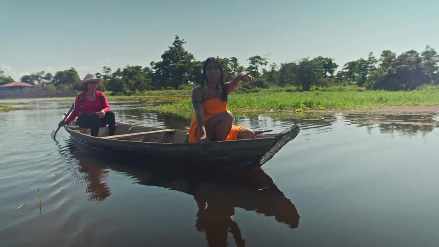 Two women navigate a small wooden boat along a calm river