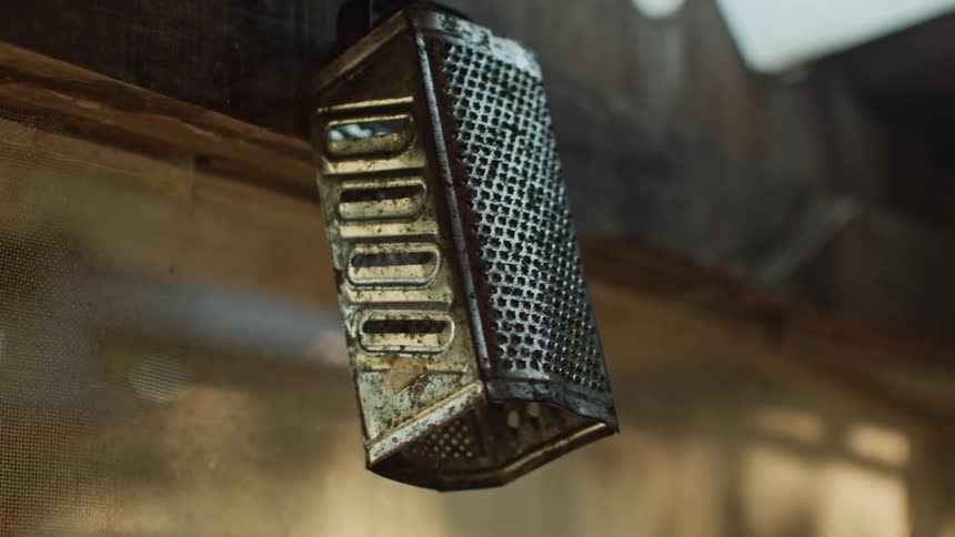 A close view of an old tarnished metal cheese grater shows it hanging from a wooden beam