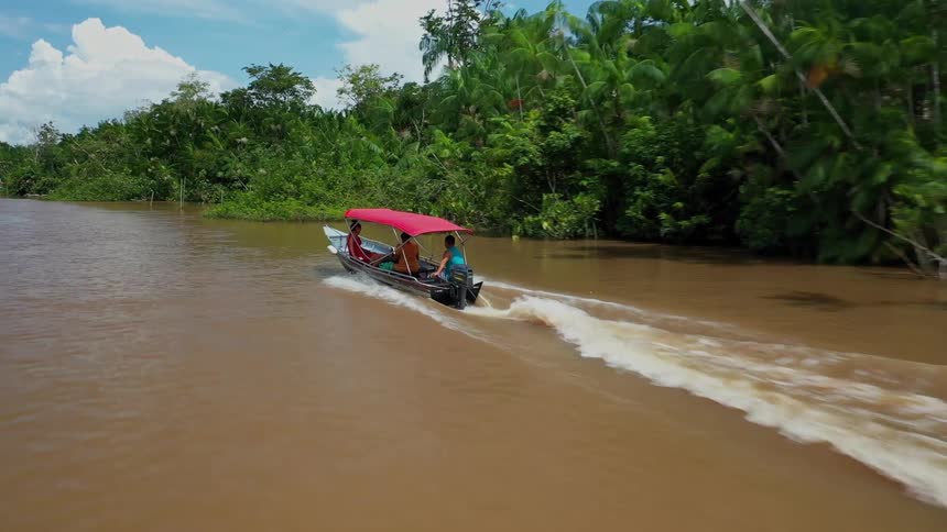 Boat speeds along a muddy river beside dense tropical forest