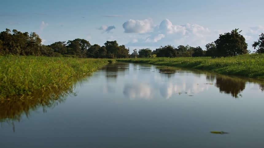 Calm river flows between grassy banks under a blue sky