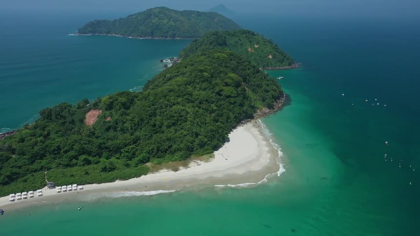 An aerial view shows a lush green peninsula bordered by turquoise waters and a white sandy beach