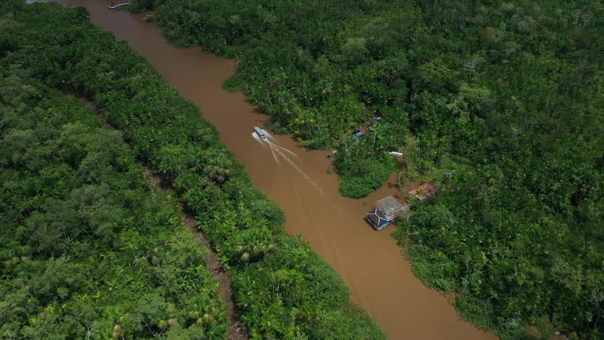 Small boat travels along a muddy river through dense green forest