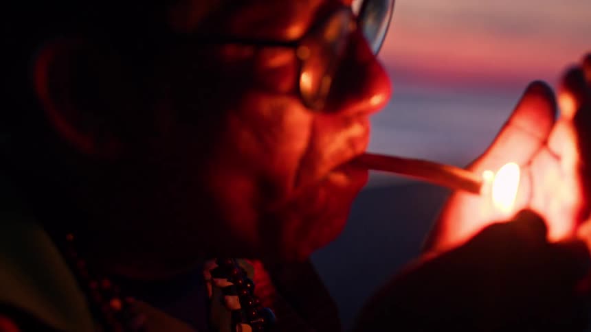 Person lights a cigarette with a lighter during sunset