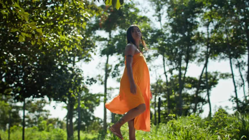 Woman walks in a wooded area wearing an orange dress