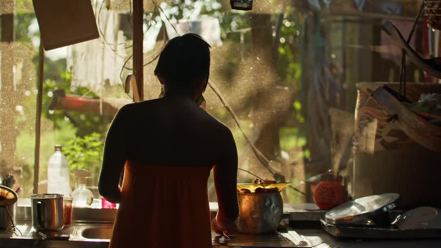 Woman washes dishes at a kitchen sink backlit by sunlight