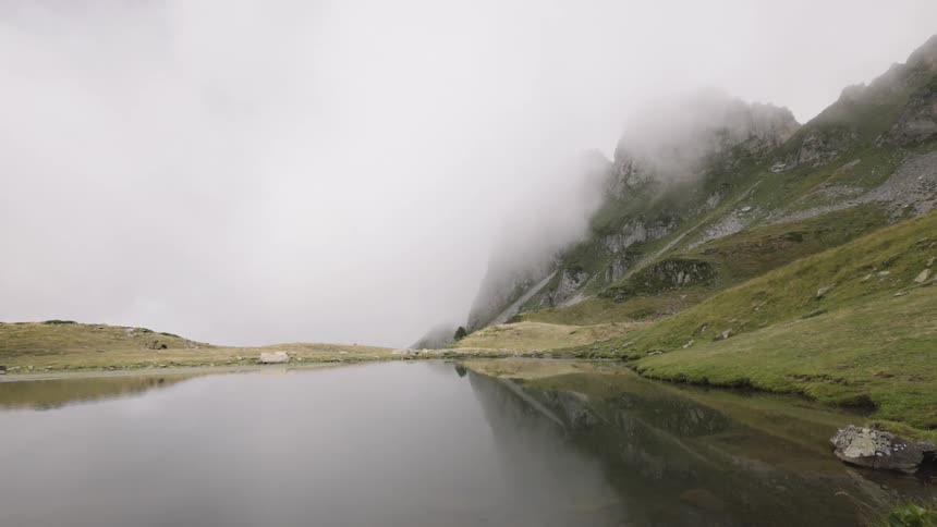 Lake reflecting mountain partially covered by mist