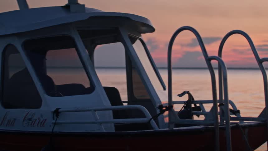 Boat with rear ladder sails on calm waters at sunset