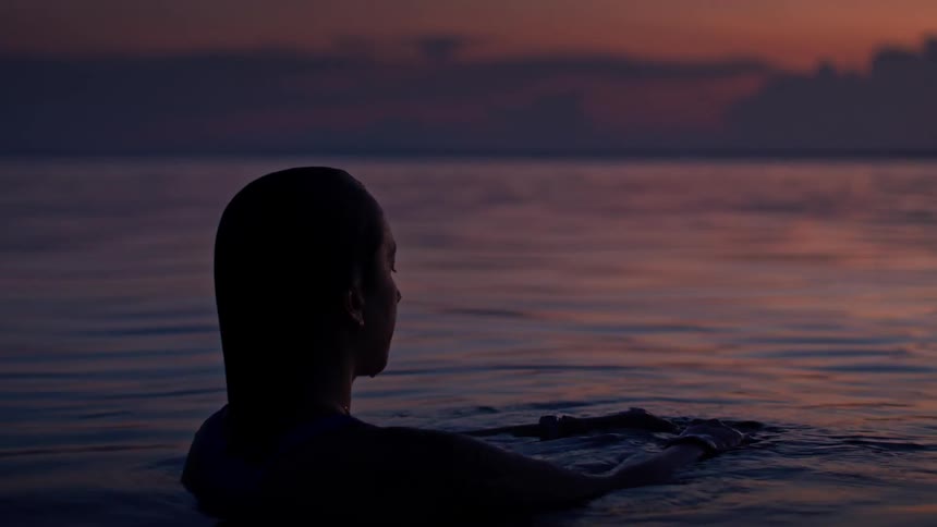 A person floats in calm ocean water at sunset