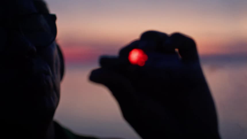 Person in silhouette holds a lit cigarette at sunset