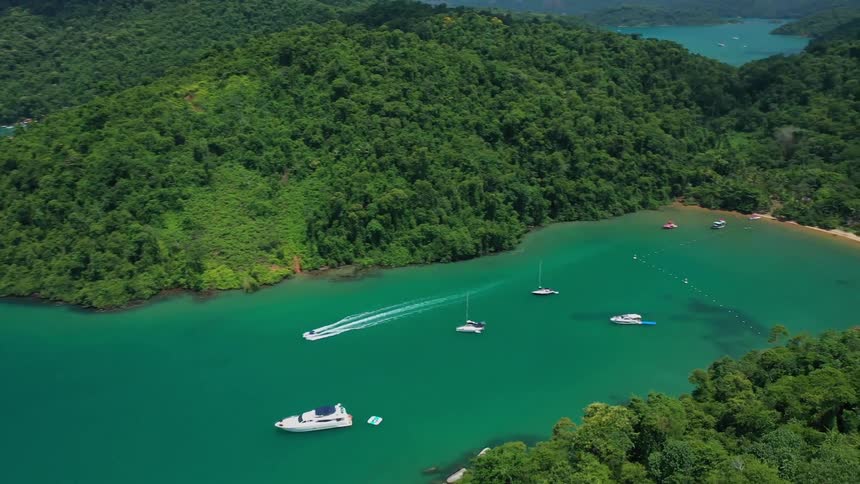A coastal island covered in rainforest with boats docked nearby at midday