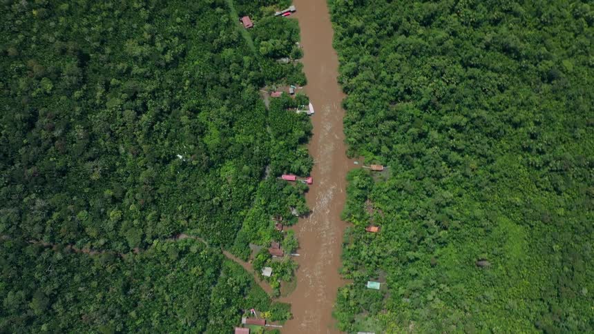 An aerial view of a winding muddy river passing through a dense forest the camera pulls back to reveal a large city on the opposite bank of the wide river showing the contrast between nature and urban life