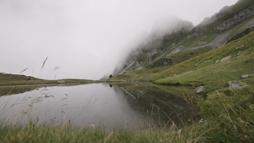 A river flows beside a grasscovered mountain at midday
