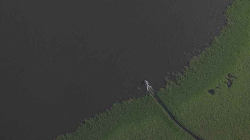 A boat rides out from a creek into a river at midday