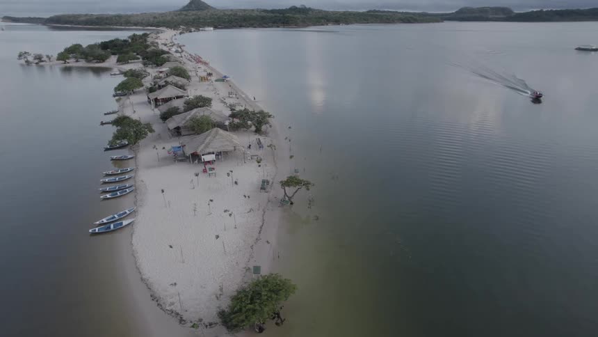 Sand strip with huts and boats surrounded by water seen from above