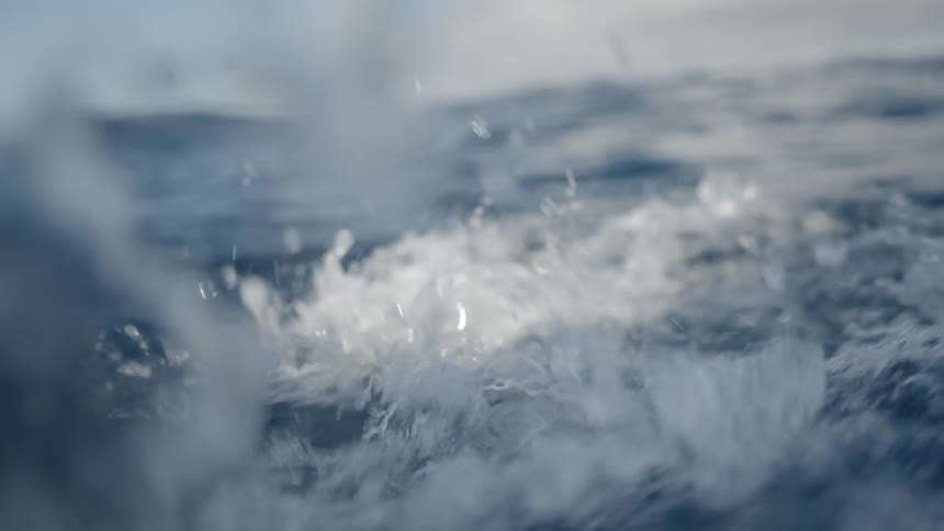 A view from a low angle shows the surface of the dark blue ocean with waves and ripples moving on top of the water