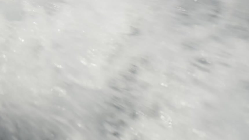 A low angle view of the dark blue ocean shows a large wave breaking in front of the camera creating a white foam of bubbles and splashes