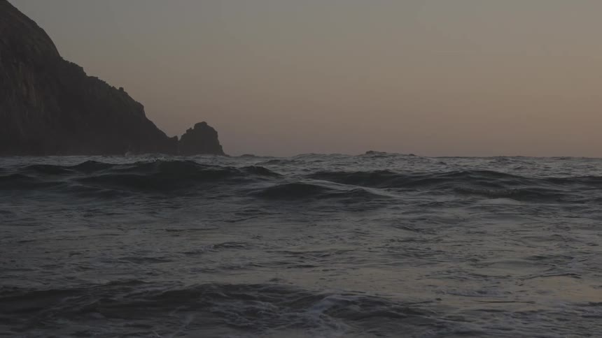 Rough waves approach the shore with cliffs in the background