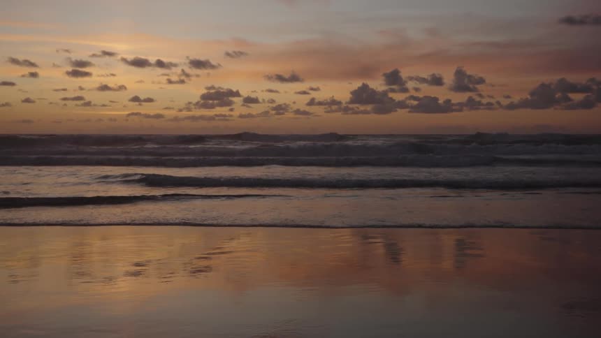 A beach with calm waters and an orange sky at sunset