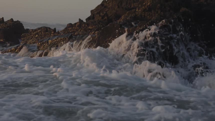 Ocean waves crash against a rock creating a splash at dawn