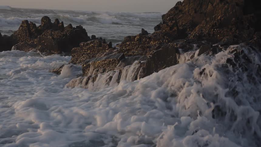 Waves crash on rocky coastal cliffs at sunset