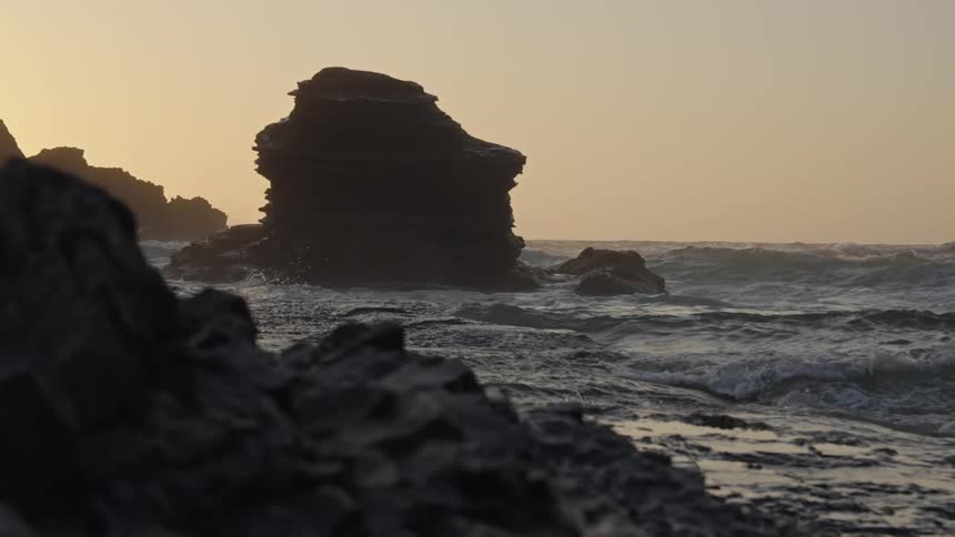 Waves crash against large sea rocks at sunset