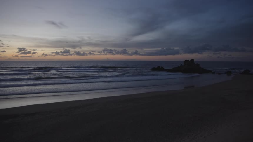 Beach with waves and a rocky outcrop at sunset