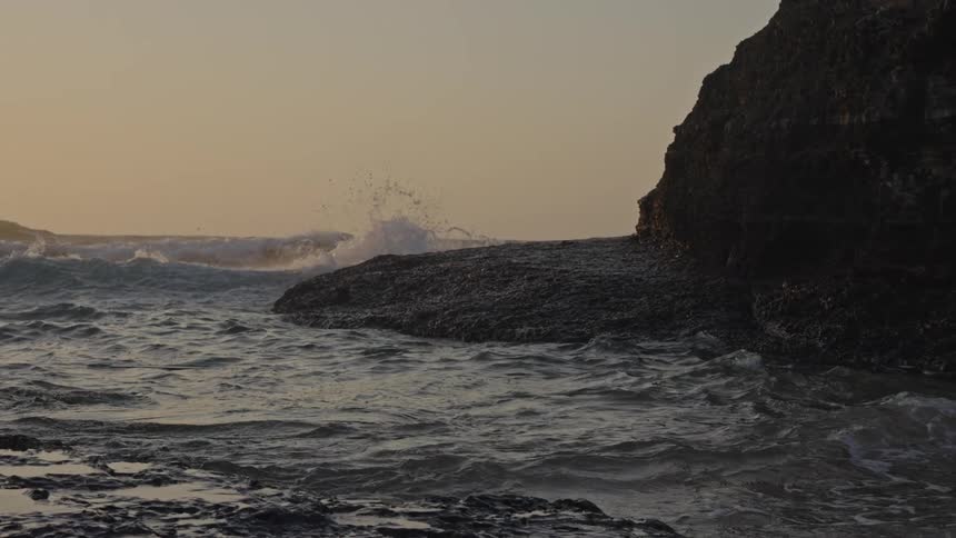 Waves crash against rocks in the sea at sunset
